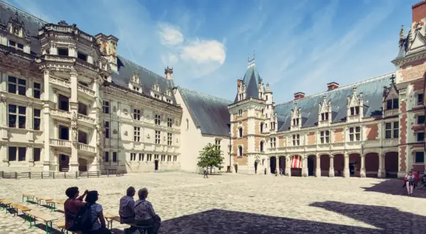 Cour intérieure du château de Blois, avec des visiteurs profitant du temps de visite. Architecture Renaissance sous un ciel bleu.