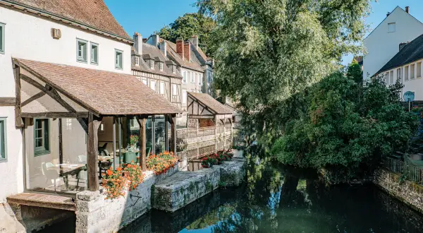 Maison ancienne au bord d'une rivière, idéale pour visiter Chartres à pied. Fleurs rouges et reflets dans l'eau.
