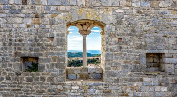 Fenêtre médiévale à Campiglia Marittima offrant une vue sur la mer et les toits du village.