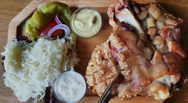Un plat tcheque copieux : un jarret de porc rôti à la peau croustillante, servi avec de la choucroute, des poivrons, des oignons rouges et deux sauces.
