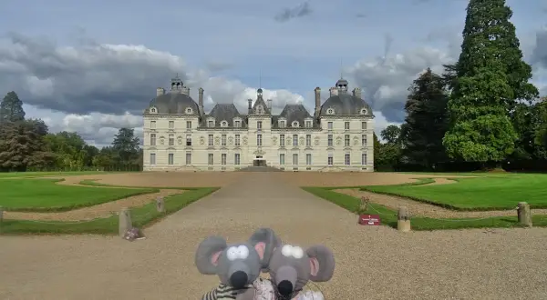 Deux souris en peluche devant le majestueux château de Cheverny, un jour de ciel nuageux.