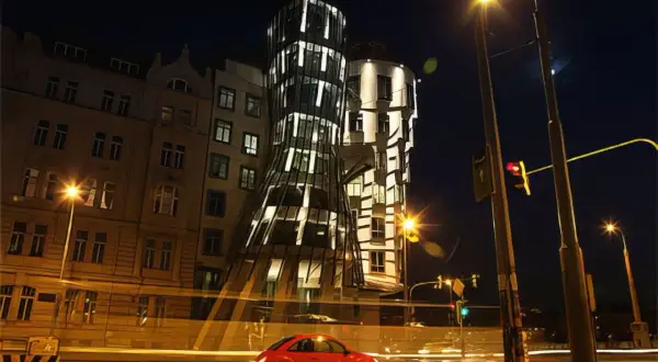 La **maison dansante Prague** s'illumine la nuit, une voiture rouge passe devant, créant une scène urbaine animée.