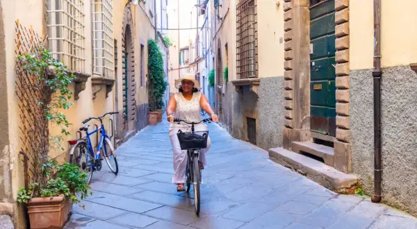 Une femme souriante fait du vélo dans une ruelle pavée, profitant d'une belle journée à Florence.