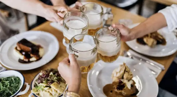 Des mains portent des chopes de bière pour trinquer, autour d'une table garnie de plats traditionnels. Un vrai petit déjeuner à Prague.