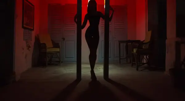 Silhouette d'une femme dans un décor rouge, évoquant l'ambiance du quartier rouge de Prague. Des chaises et des portes bleues créent un contraste saisissant.