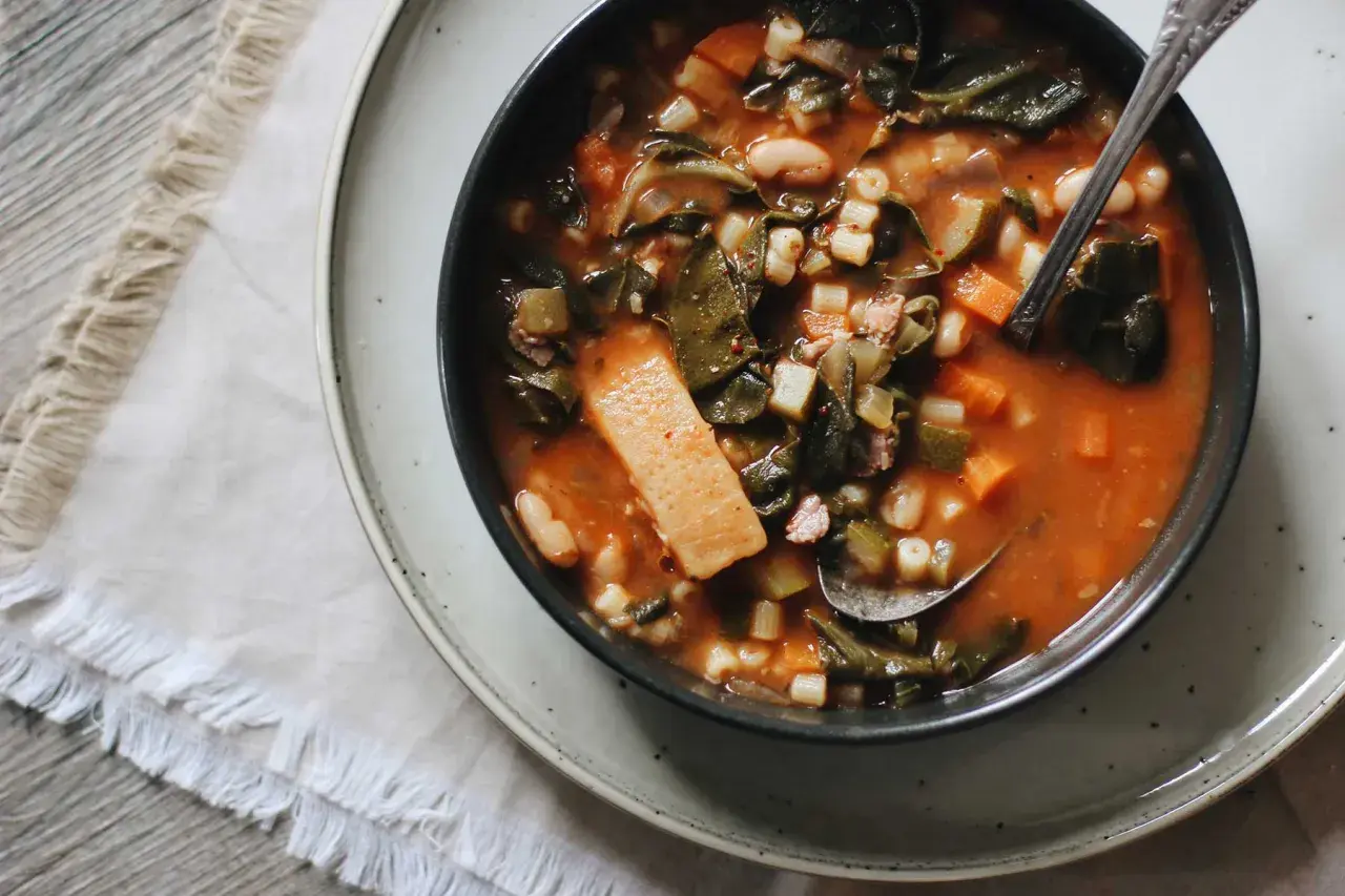 Un bol de ribollita toscana, une soupe épaisse et réconfortante avec des légumes verts, des haricots et des pâtes, servie avec une cuillère.