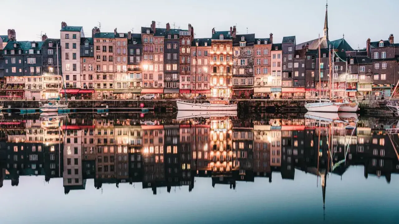 Les maisons colorées de Honfleur se reflètent dans l'eau calme, parfait pour un weekend. Bateaux amarrés, lumières douces.