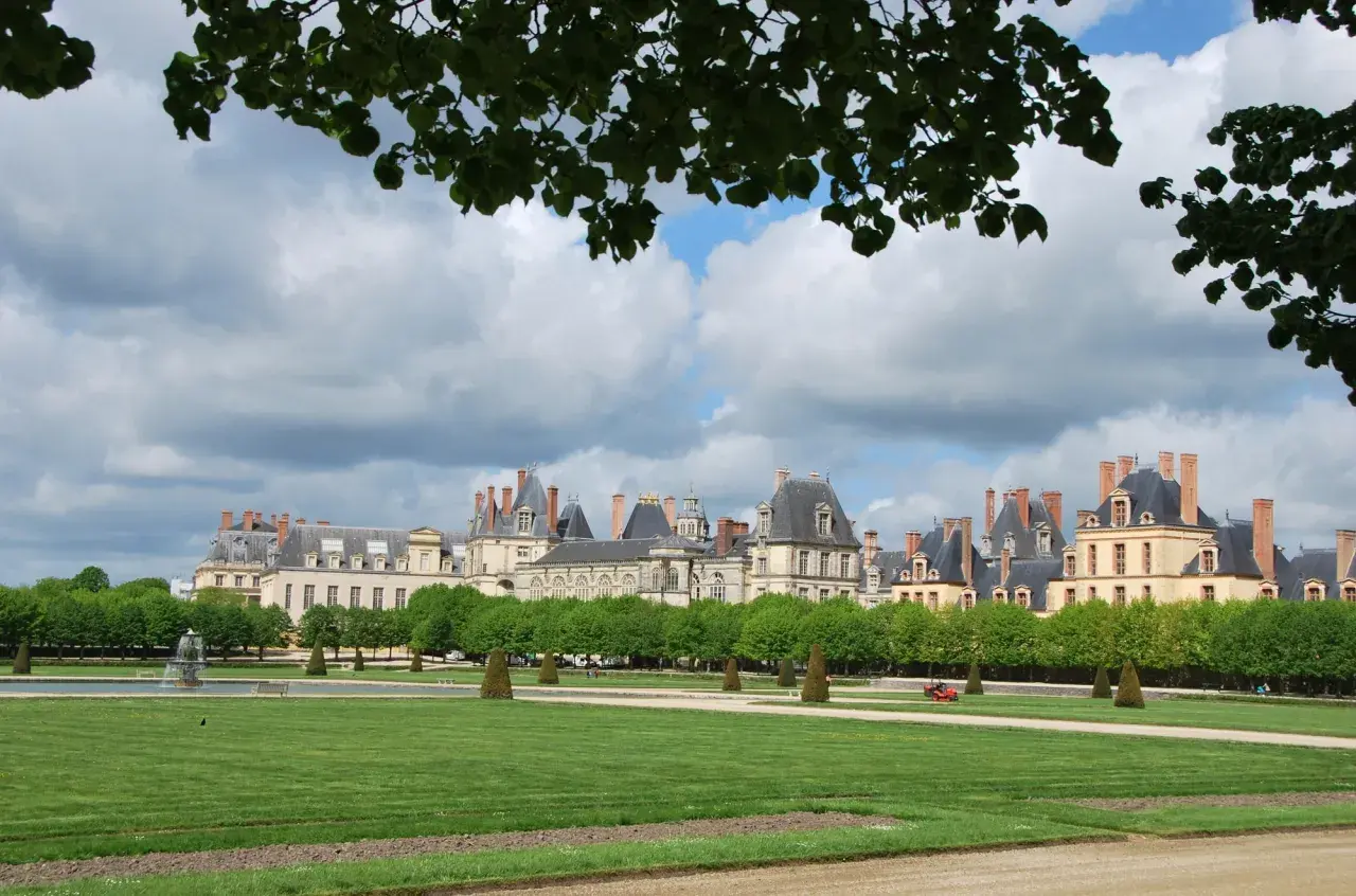 Magnifique vue du château de Fontainebleau, idéal pour visiter. Pelouse verdoyante, fontaine et arbres taillés.