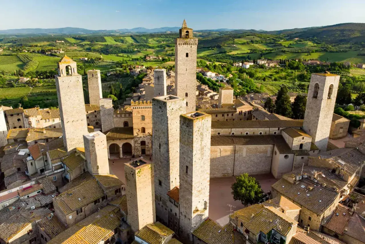 Vue aérienne de San Gimignano, avec ses tours médiévales emblématiques se dressant au-dessus des toits de tuiles, le tout baigné par la lumière dorée du soleil toscan.