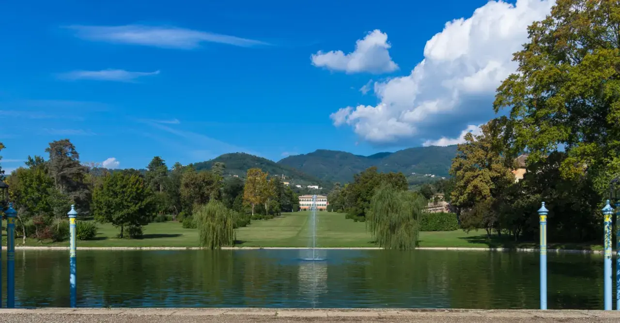 Le parc de la villa reale di Marlia s'étend devant un étang paisible, avec une fontaine jaillissant au centre. Des arbres majestueux bordent la pelouse menant à la villa.