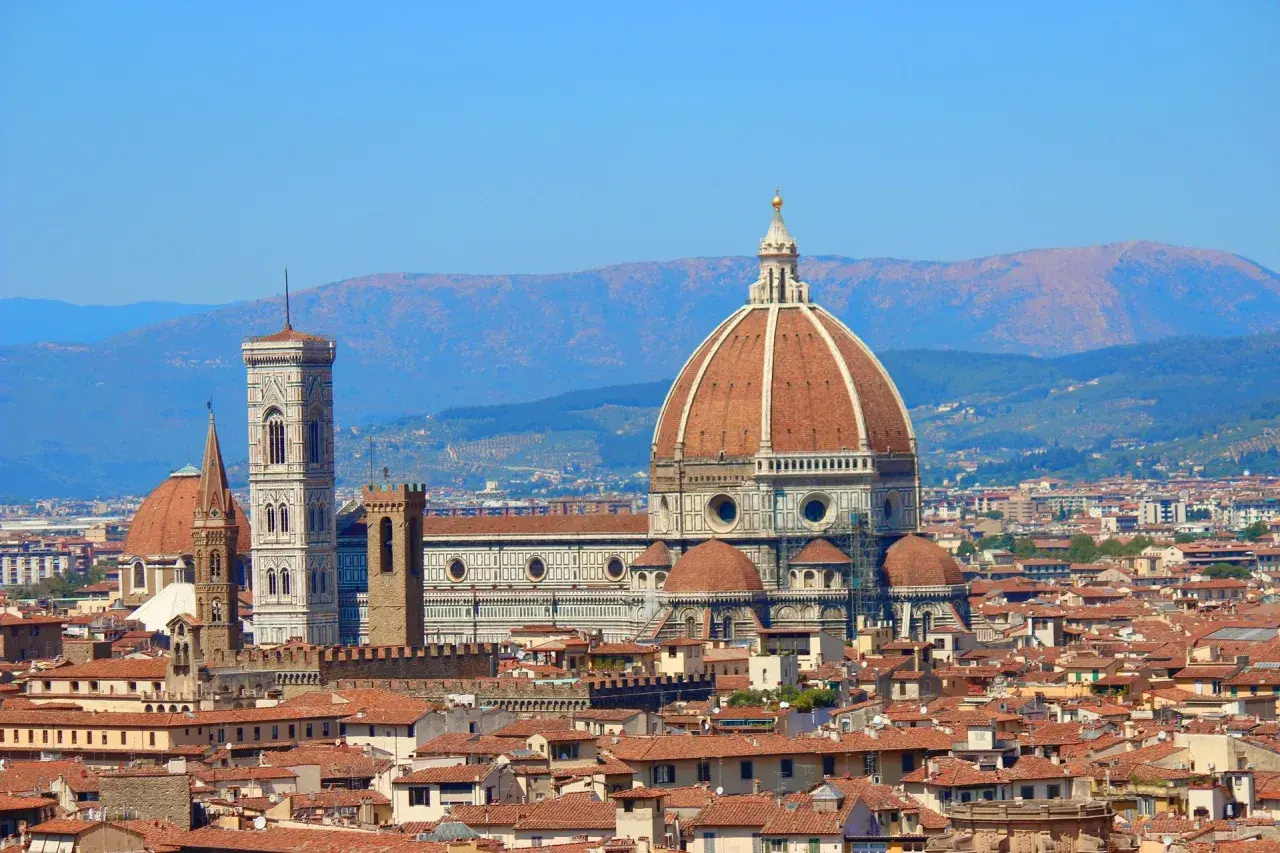 La célèbre coupole de Florence domine la ville, avec son campanile et ses toits de tuiles rouges sous un ciel bleu.