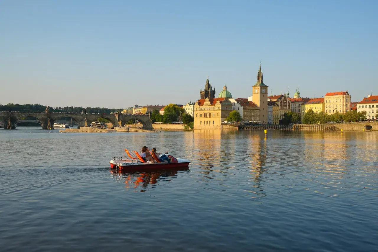 Un couple profite d'une balade en pédalo sur la Vltava, offrant une perspective insolite de Prague et de son pont emblématique au coucher du soleil.