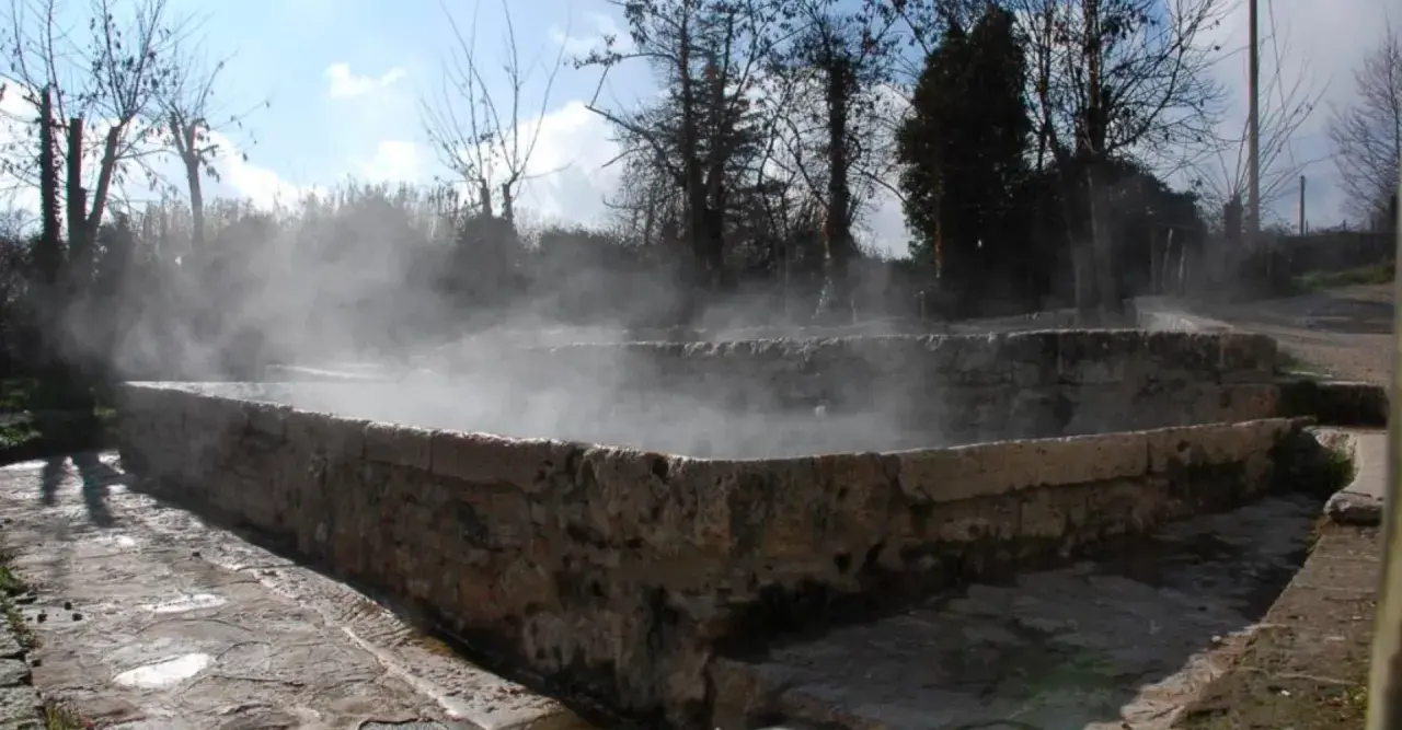 Bains antiques en pierre à San Casciano dei Bagni, dégageant une vapeur d'eau chaude sous un ciel bleu.