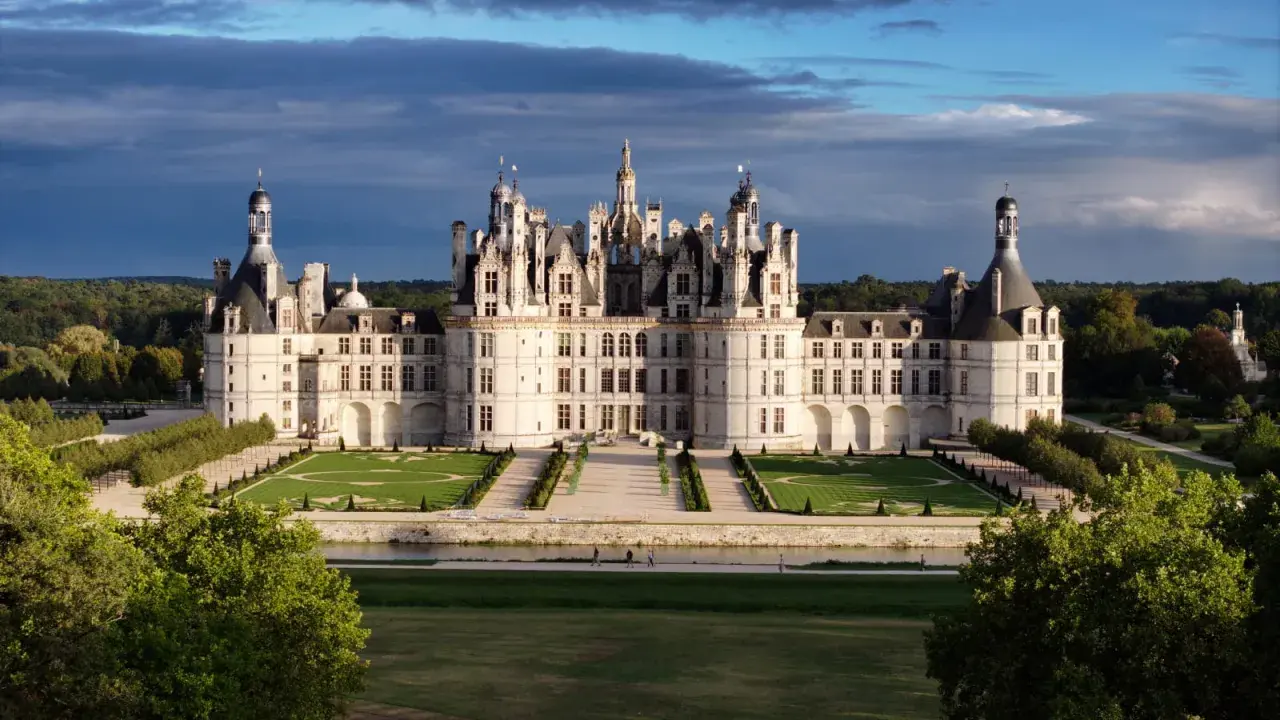 Le majestueux château de Chambord se dresse, avec ses tours et ses toits complexes, sous un ciel dramatique.