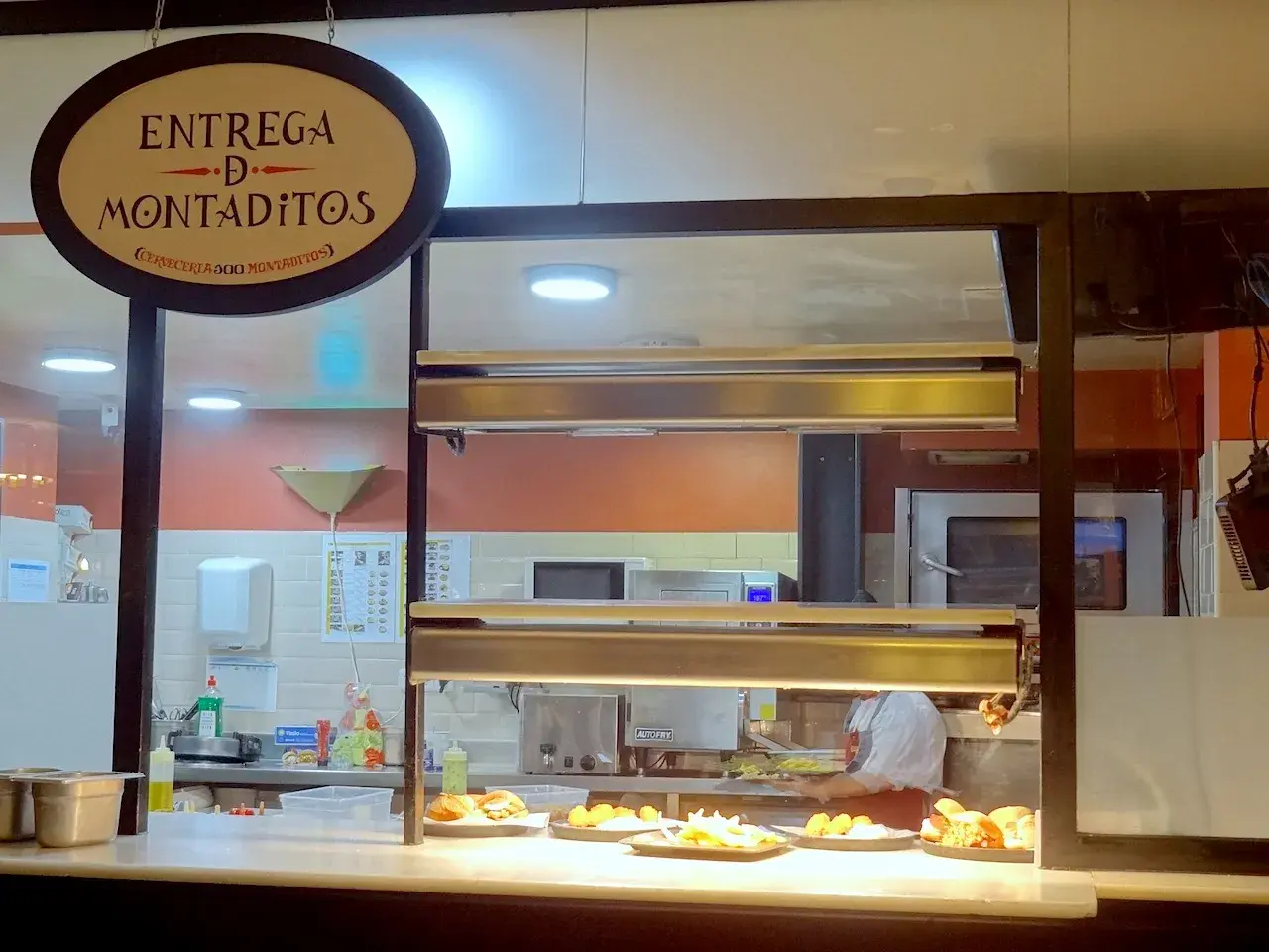 Un comptoir de restaurant à Madrid, avec un panneau "Entrega de Montaditos". Des plats appétissants sont exposés, parfaits pour savoir où manger à Madrid.