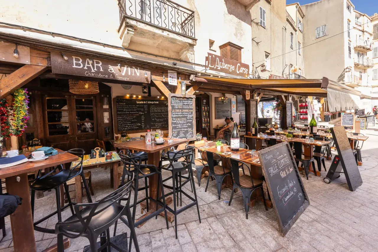 Terrasse d'un restaurant "Bar à Vin" dans le restaurant bonifacio vieille ville. Tables dressées, chaises noires, ardoises de menu. Ambiance estivale.