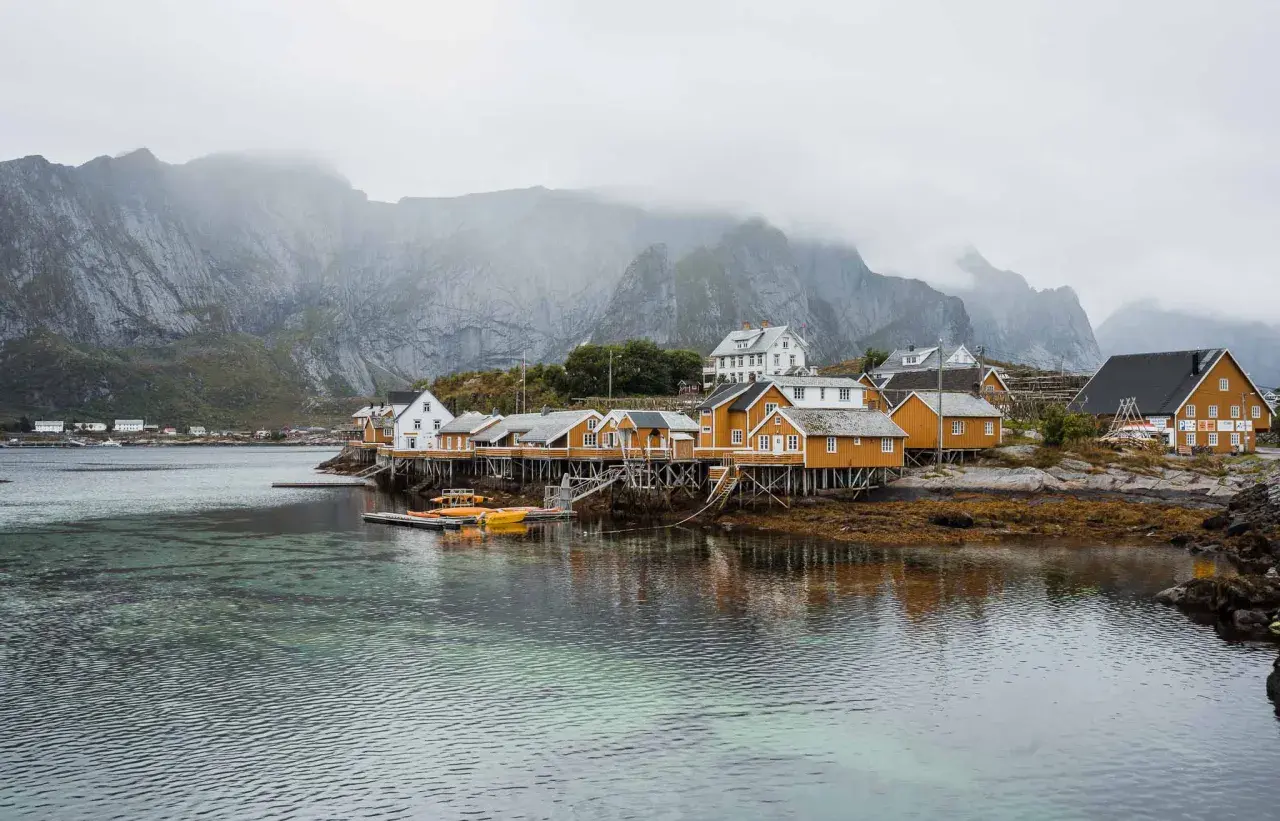Maisonnettes jaunes sur pilotis, reflets dans l'eau, montagnes brumeuses en arrière-plan. Idéal pour un budget voyage îles Lofoten.