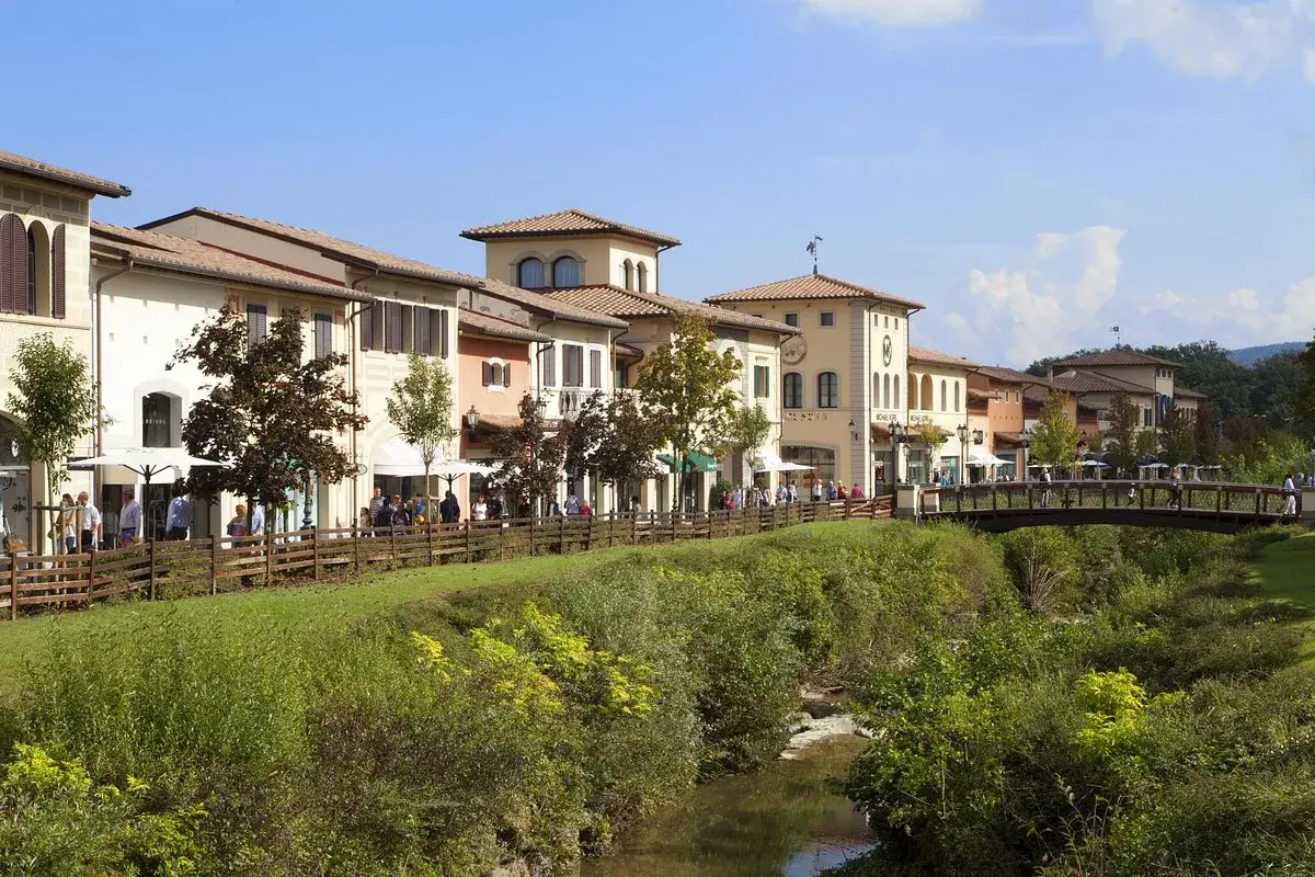 Boutiques colorées le long d'une rivière à Barberino di Mugello, avec des passants sur un pont en bois.