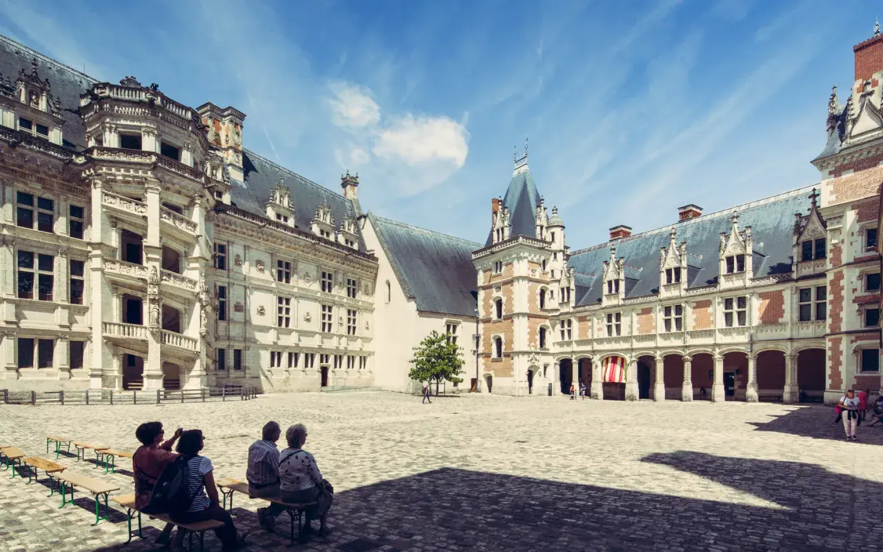 Cour intérieure du château de Blois, avec des visiteurs profitant du temps de visite. Architecture Renaissance sous un ciel bleu.