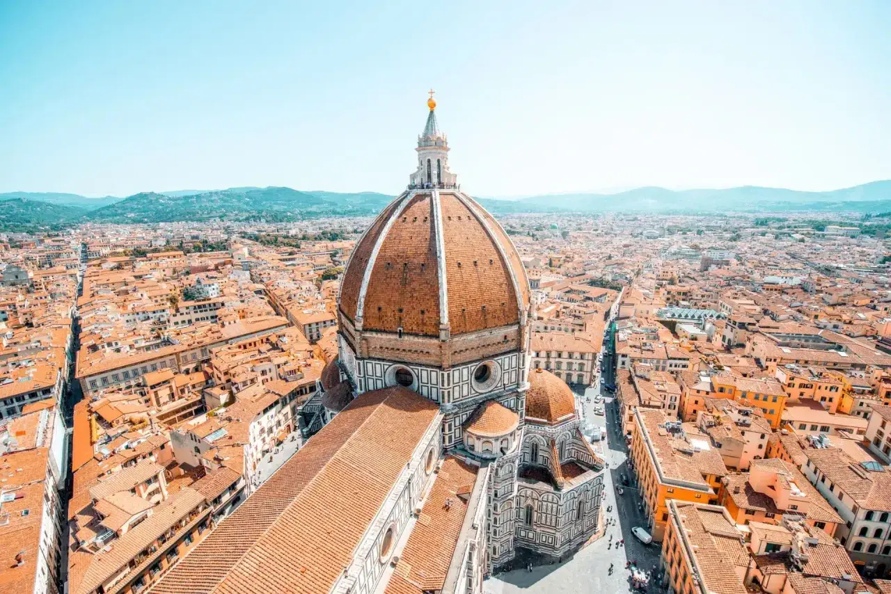 Vue aérienne de Florence, avec le dôme de Brunelleschi dominant la ville. Les toits de tuiles orangées s'étendent à perte de vue.