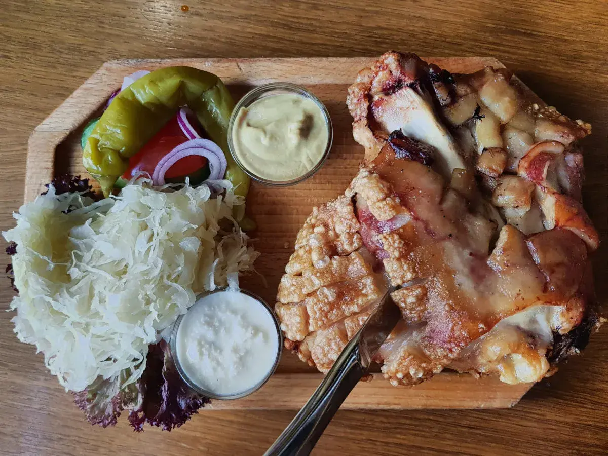 Un plat tcheque copieux : un jarret de porc rôti à la peau croustillante, servi avec de la choucroute, des poivrons, des oignons rouges et deux sauces.