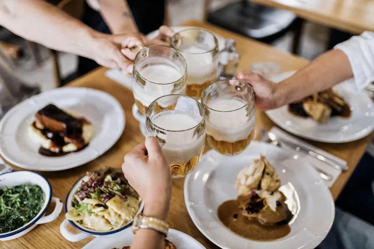 Des mains portent des chopes de bière pour trinquer, autour d'une table garnie de plats traditionnels. Un vrai petit déjeuner à Prague.