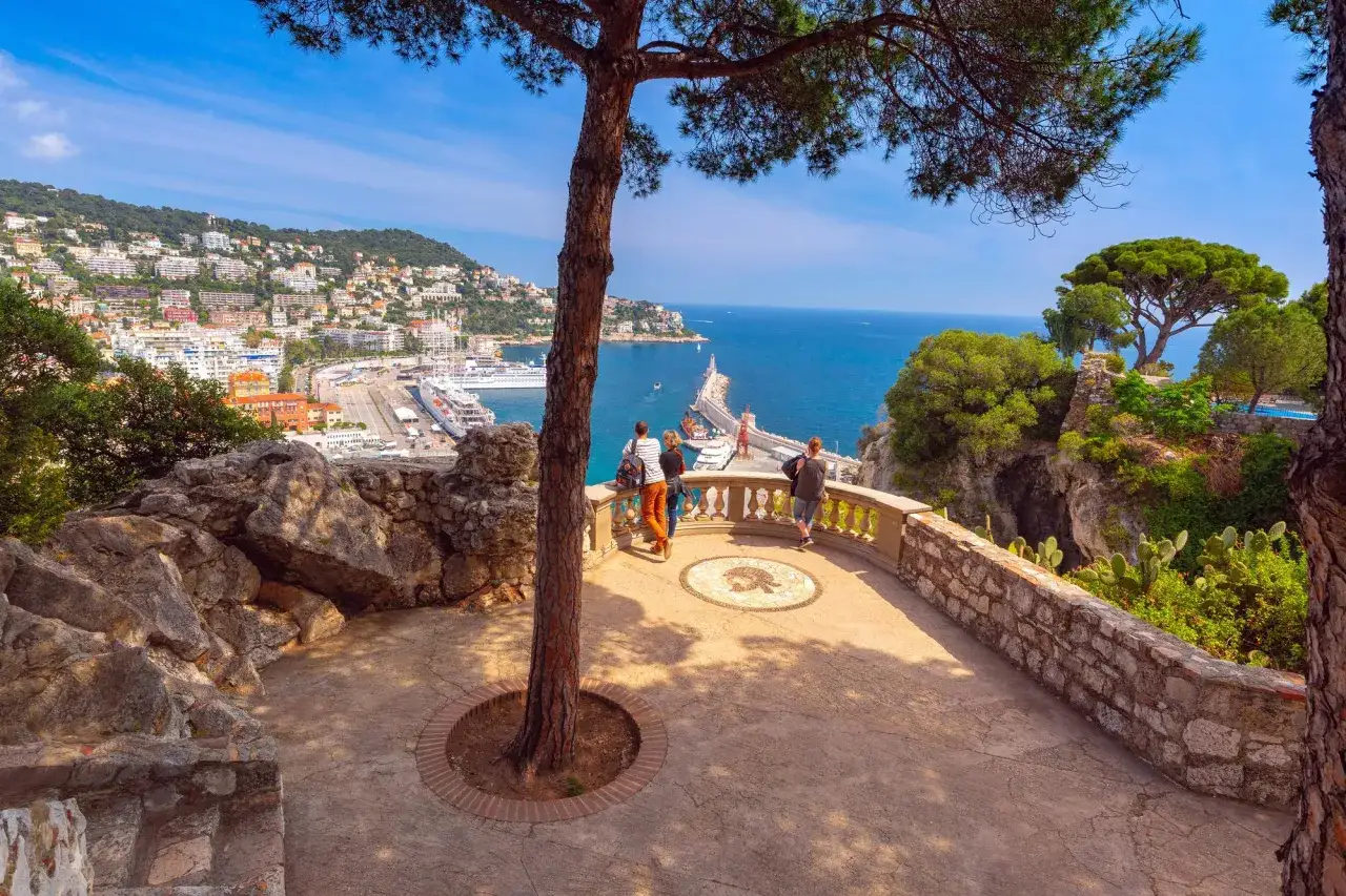 Vue panoramique sur le port de Nice, avec des bateaux de croisière. Un couple profite d'un week end nice sur la terrasse.