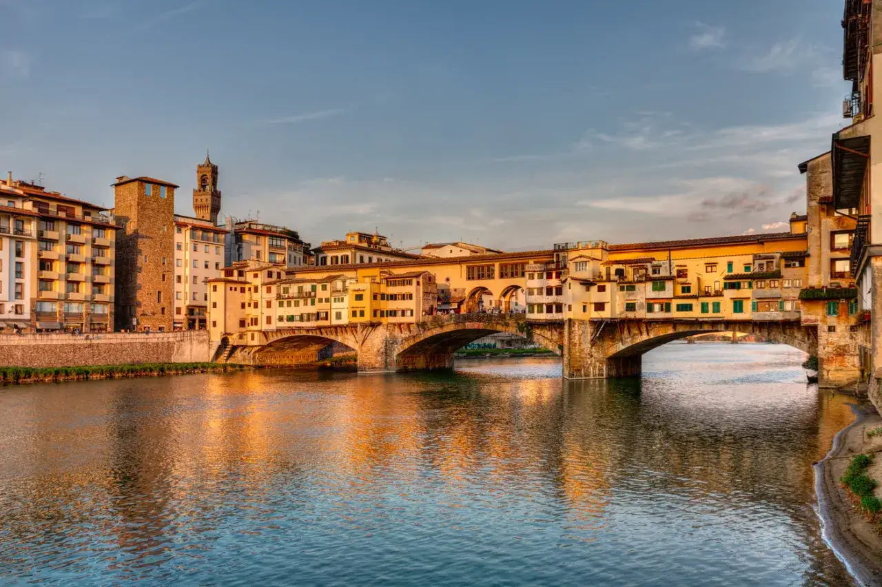 Le Ponte Vecchio de Florence, baigné par la lumière dorée du soleil couchant, se reflète sur l'Arno. Ses boutiques pittoresques semblent flotter sur l'eau.