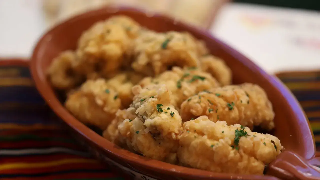Délicieux beignets de poisson, spécialité du restaurant Madère, servis dans un plat en terre cuite, parsemés de persil frais.