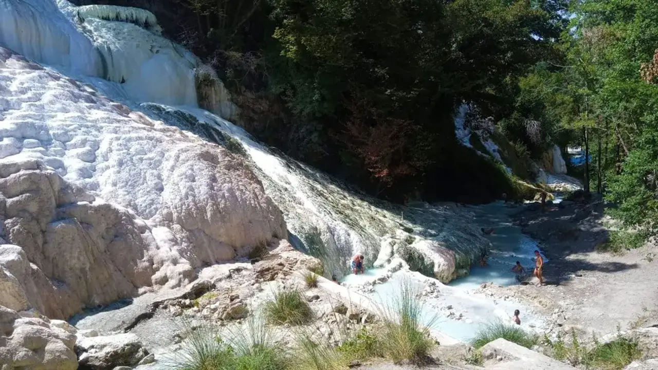 Cascades d'eau thermale aux formations calcaires blanches à San Casciano dei Bagni, où des baigneurs profitent de l'eau bleue turquoise.
