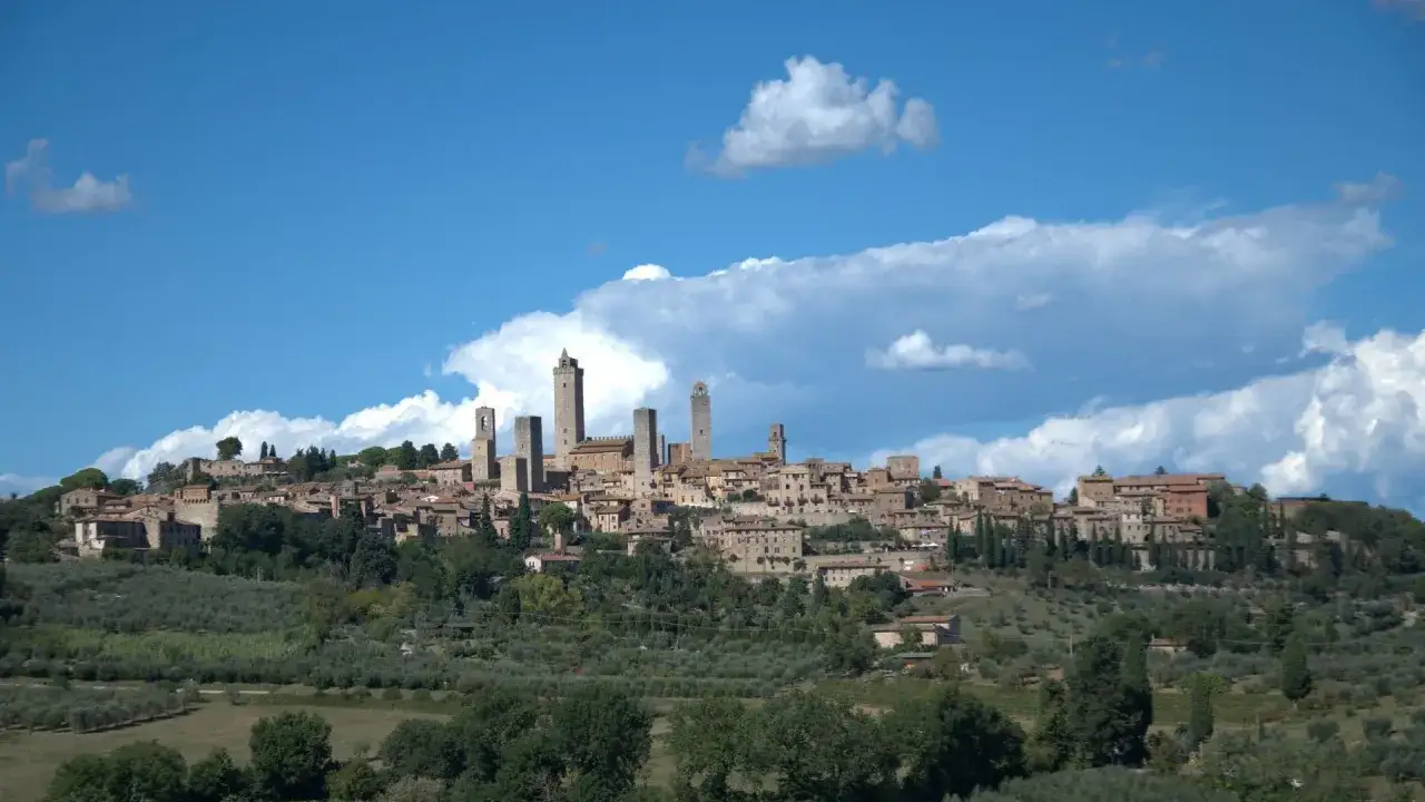 Vue panoramique de San Gimignano, ville médiévale toscane aux célèbres tours, perchée sur une colline verdoyante sous un ciel bleu et nuageux.