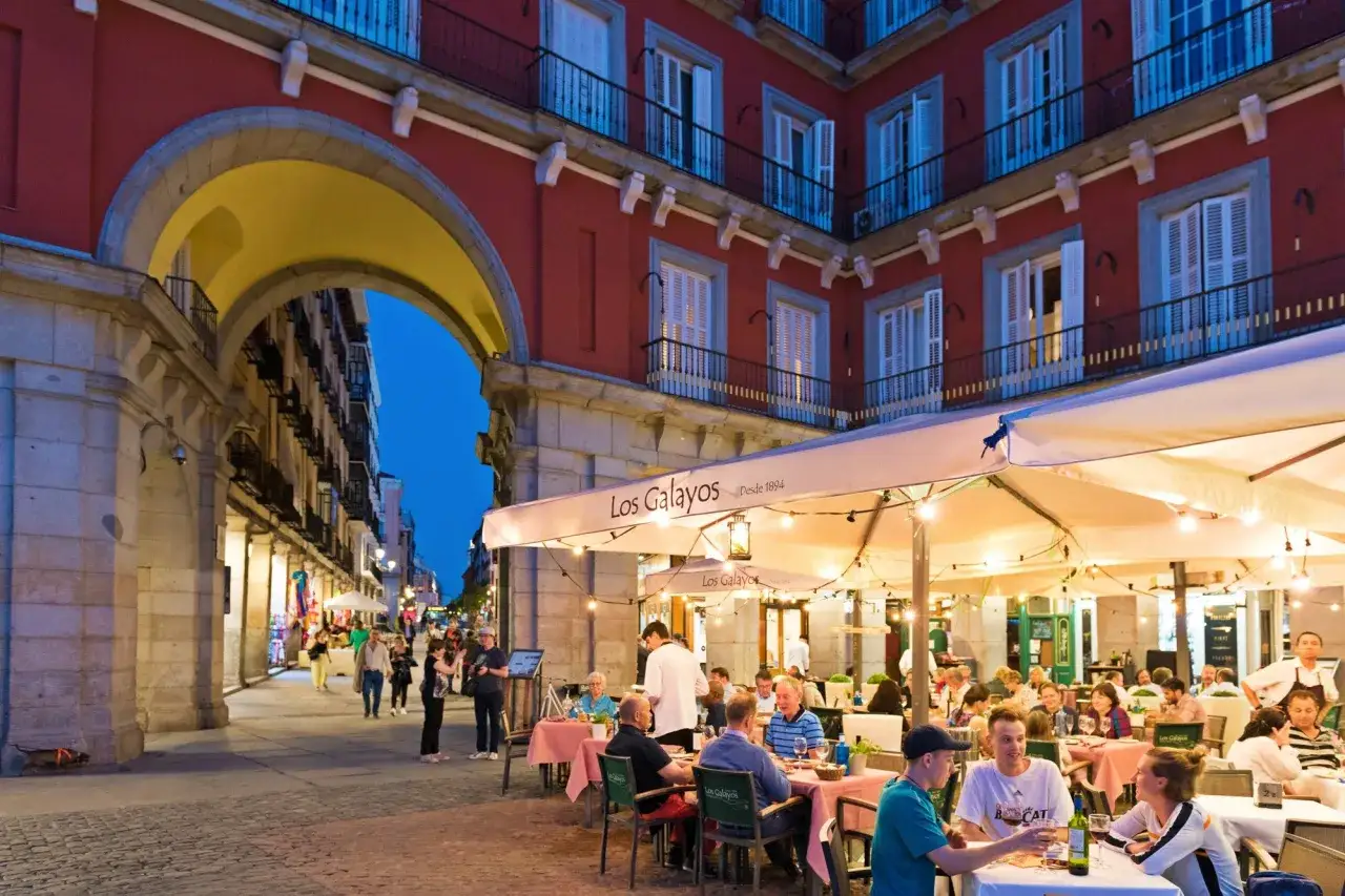 Terrasse animée de Los Galayos, un endroit idéal pour manger à Madrid. Des gens dînent sous des parasols éclairés par des guirlandes lumineuses.