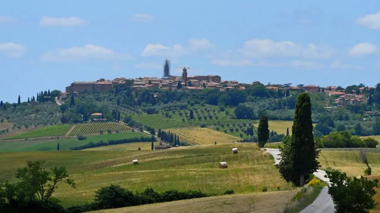 Paysage toscan avec Pienza en arrière-plan, vignobles, champs de blé et balles de foin.