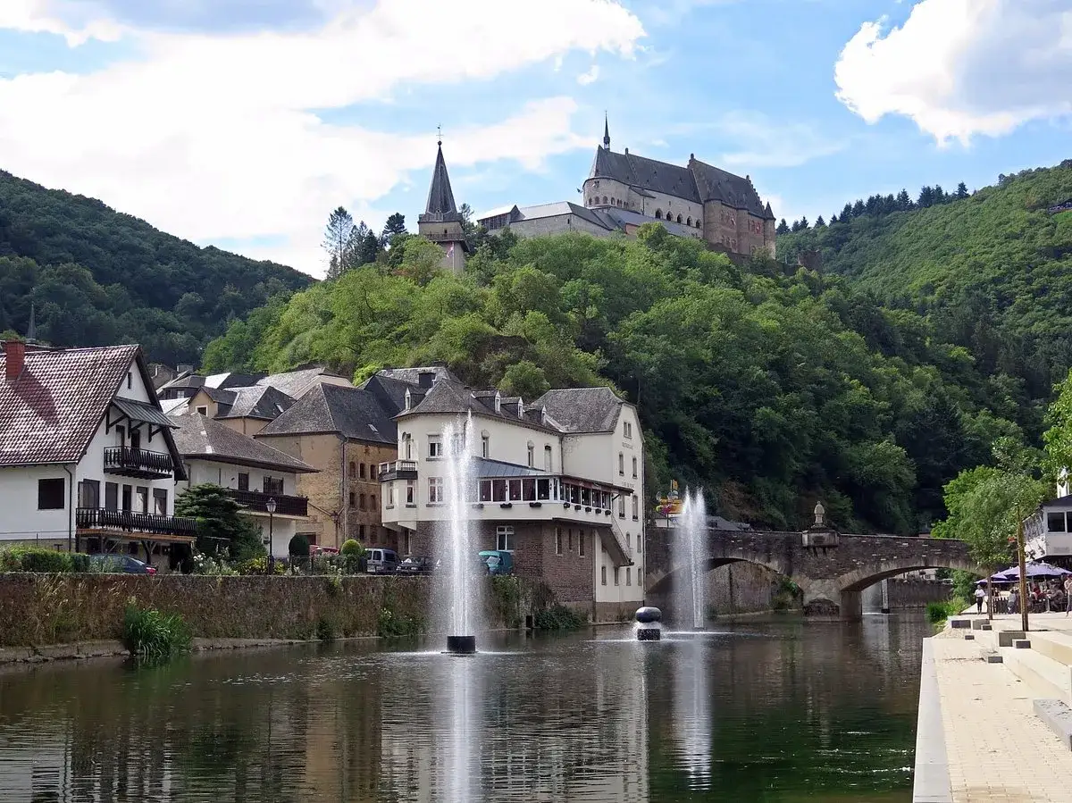 Idéal pour visiter le Luxembourg en 3 jours : un château médiéval surplombe un village pittoresque avec des fontaines dans la rivière.