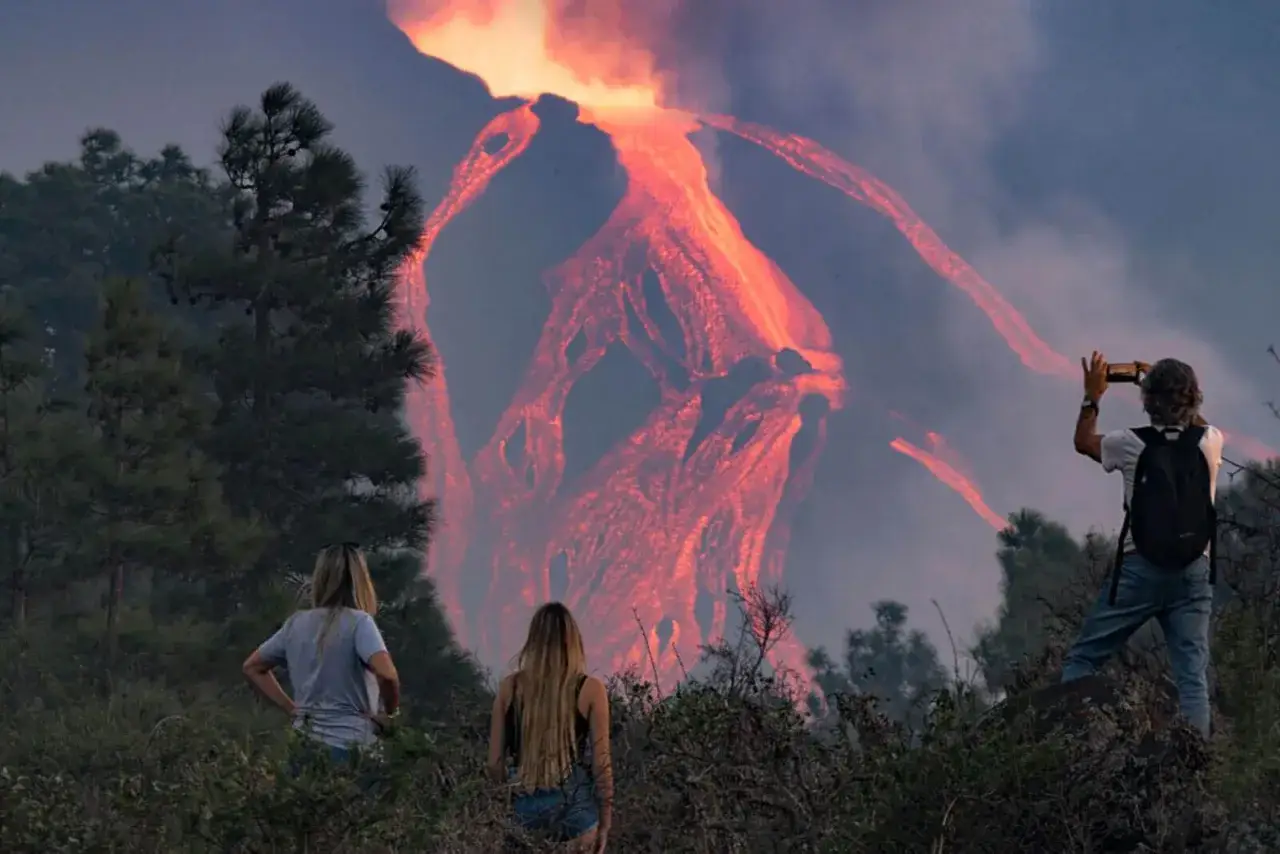 Des spectateurs observent la lave incandescente couler du volcan sur la Palma. Un homme prend une photo avec son téléphone.