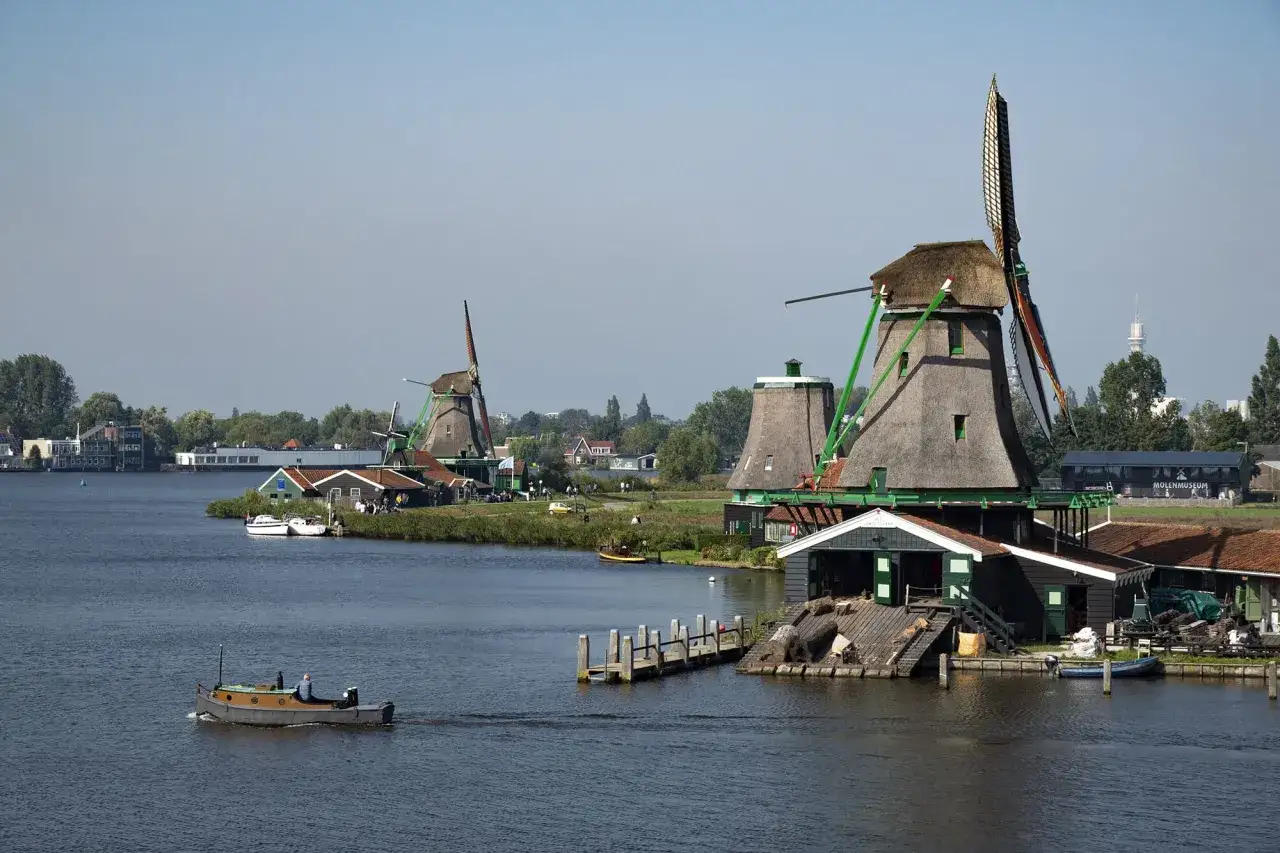 Moulins à vent traditionnels sur l'eau, un bateau navigue. Idéal pour savoir quoi visiter en Hollande.