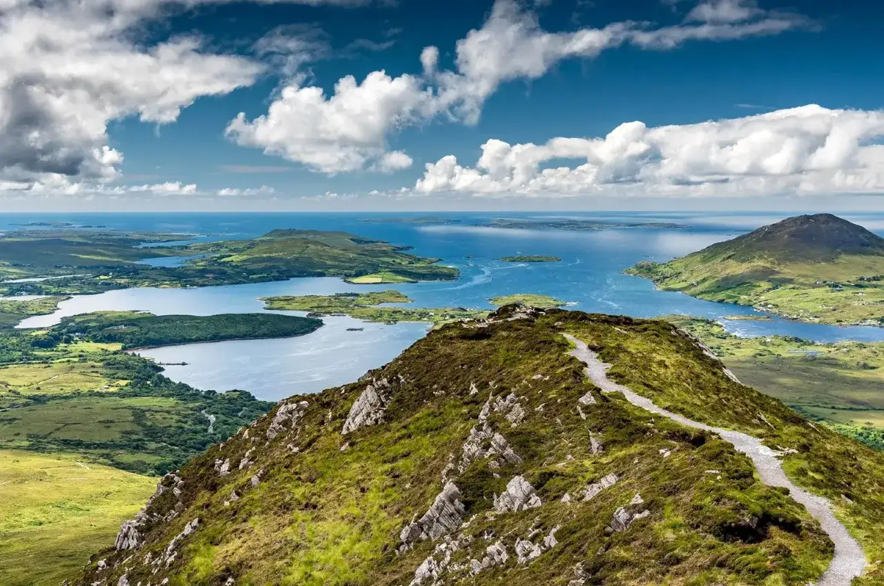 Sentier de randonnée sur une colline verdoyante offrant une vue panoramique sur les lacs et l'océan, une parfaite visite du Connemara depuis Galway.