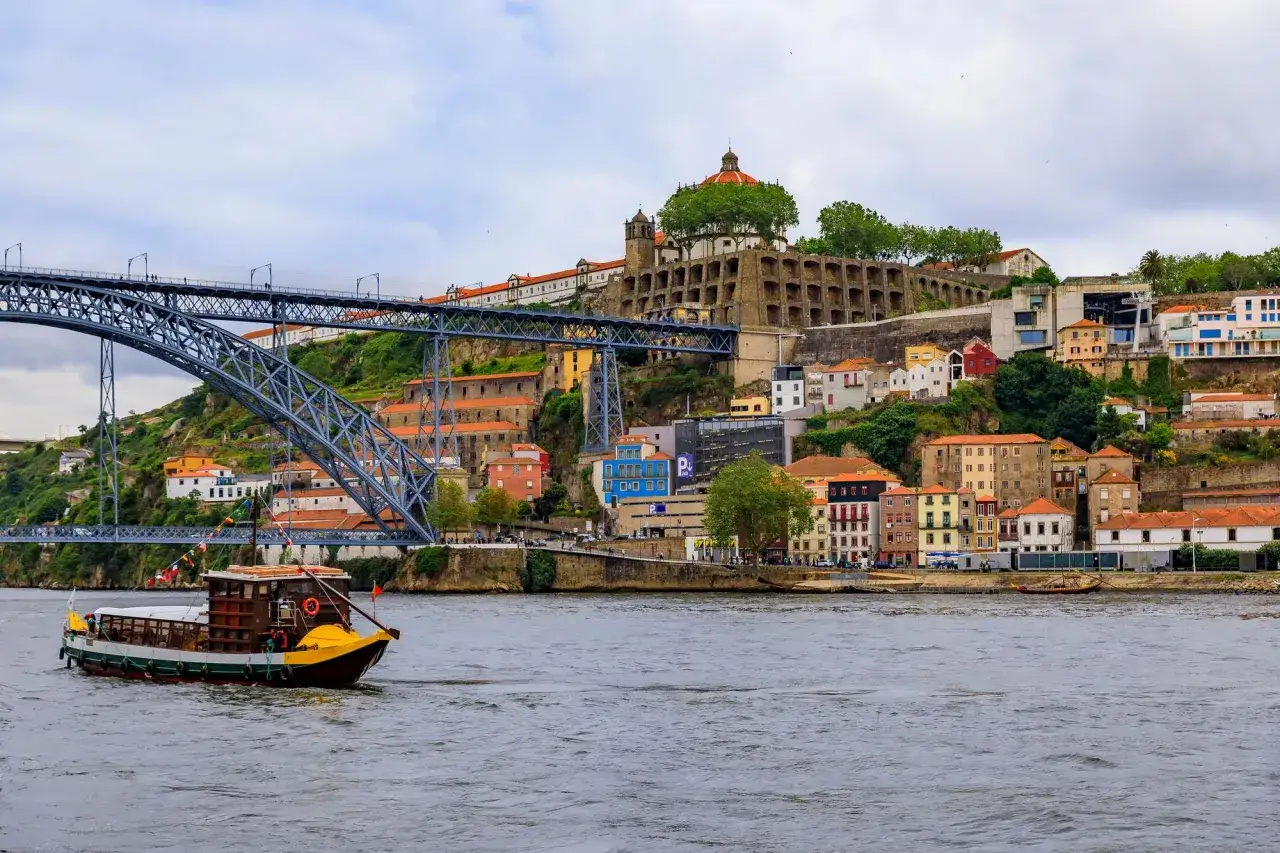 Un bateau navigue sur le Douro, sous le pont Dom-Luís I, avec les maisons colorées de Porto en arrière-plan. Un week-end à Porto inoubliable.