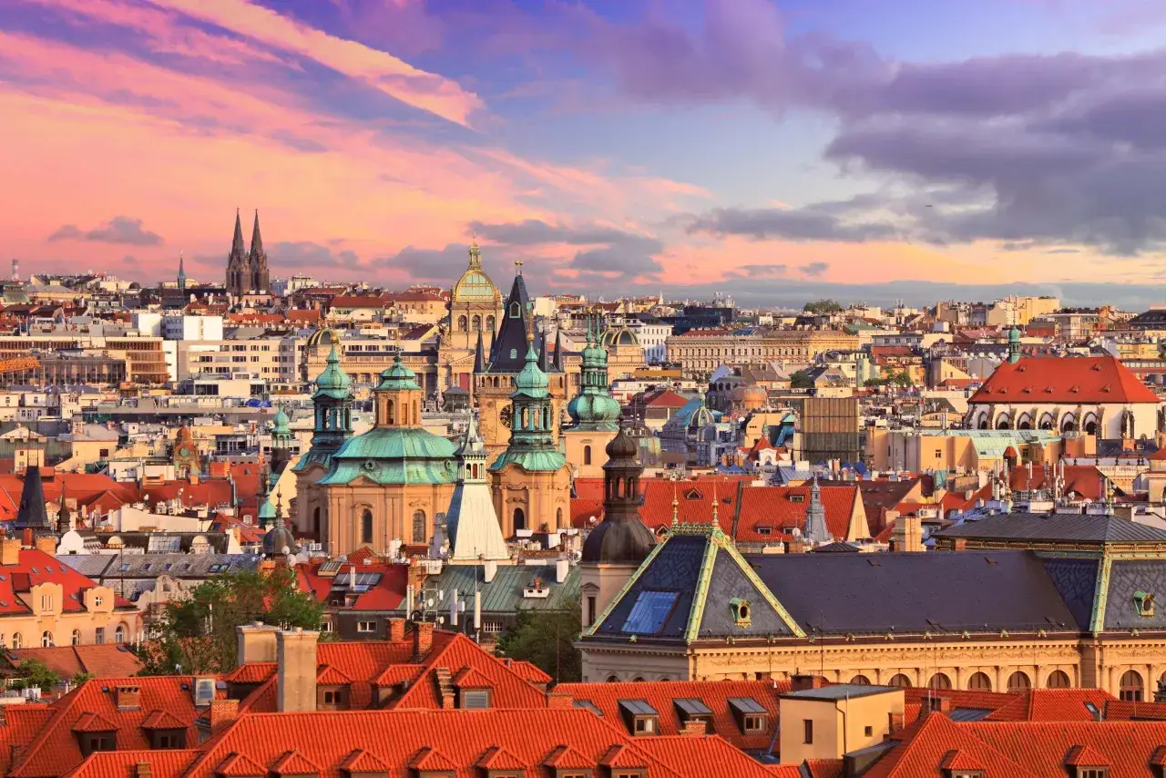 Vue panoramique de Prague au coucher du soleil, avec ses dômes verts et ses toits rouges. Un spectacle à ne pas manquer pour savoir que voir à Prague.