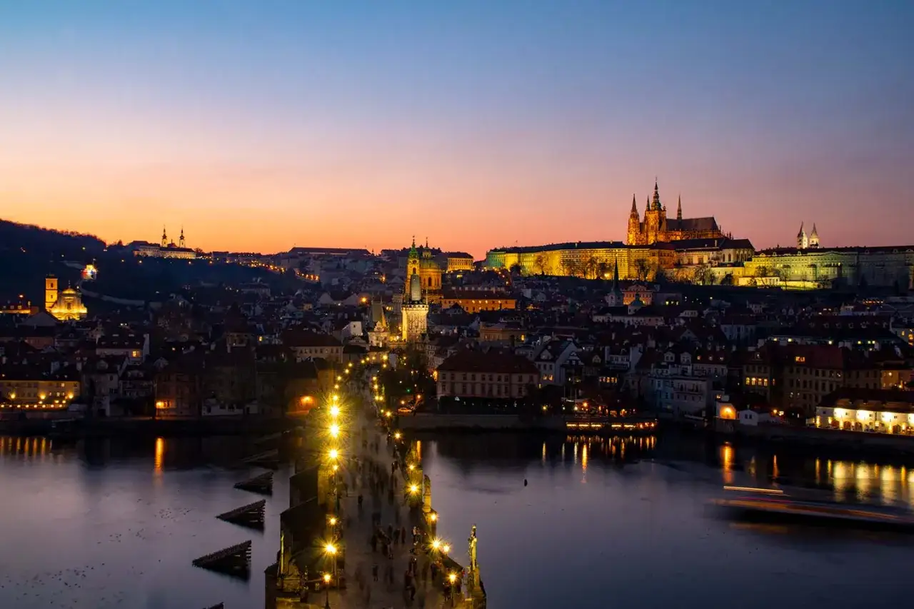 Vue panoramique de Prague au crépuscule, avec le château illuminé et le pont Charles animé. Une vue magique depuis un rooftop.