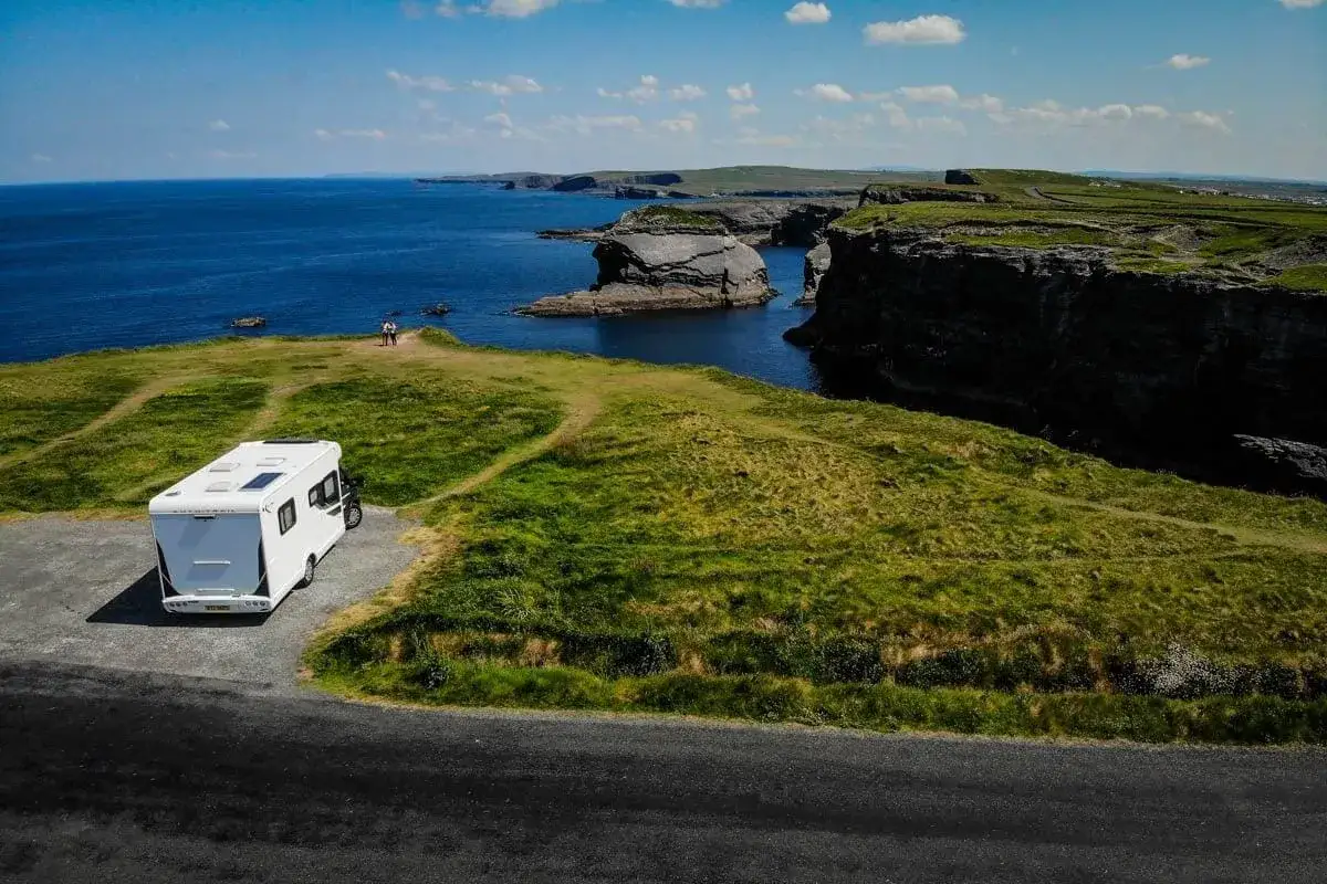 Un camping-car blanc profite d'une vue imprenable sur la côte irlandaise, avec des falaises spectaculaires et l'océan bleu.