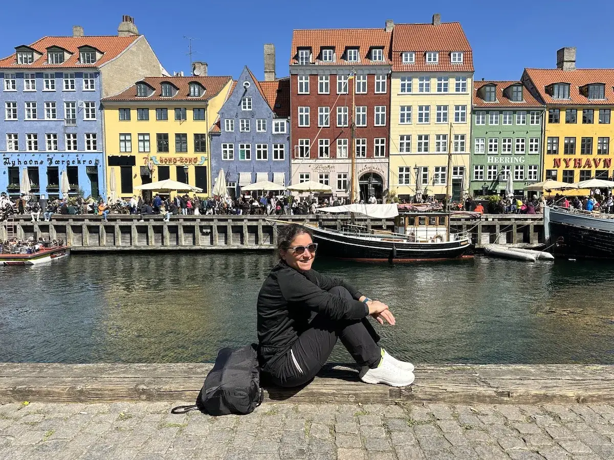 Un week-end à Copenhague, au bord des canaux colorés de Nyhavn. Une femme profite du soleil, entourée de bateaux et de façades pittoresques.