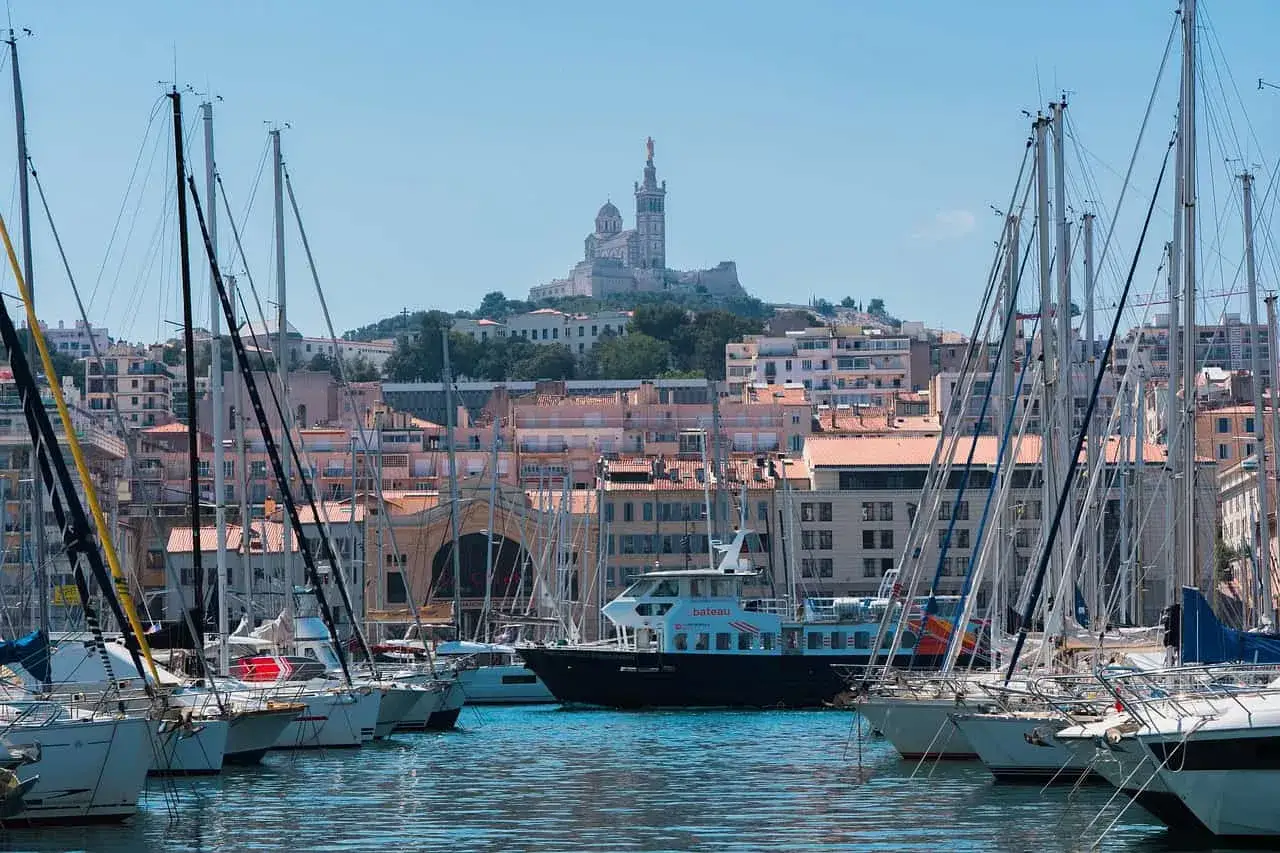 Port de Marseille avec voiliers et la basilique Notre-Dame de la Garde en arrière-plan. Idéal pour savoir que faire à Marseille ce week-end.