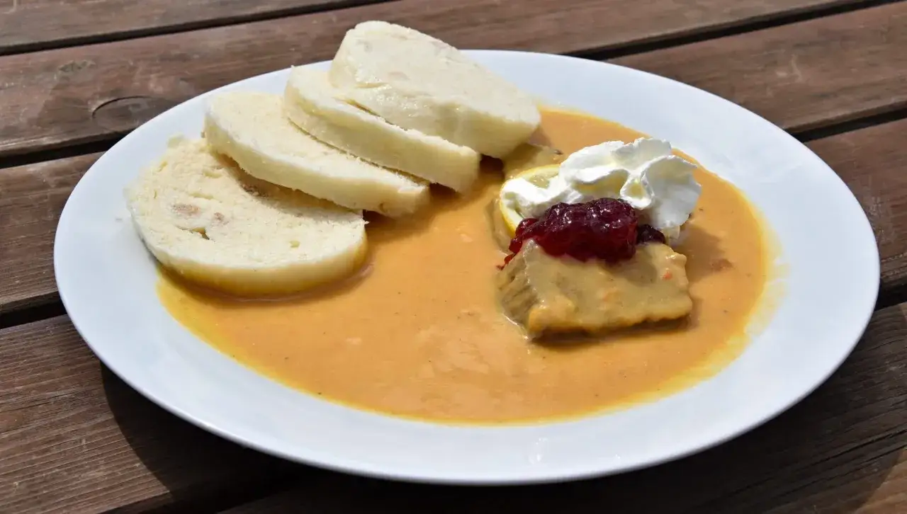 Un plat tcheque savoureux : des tranches de pain, une viande en sauce onctueuse, garni de crème fouettée et de confiture de fruits rouges.