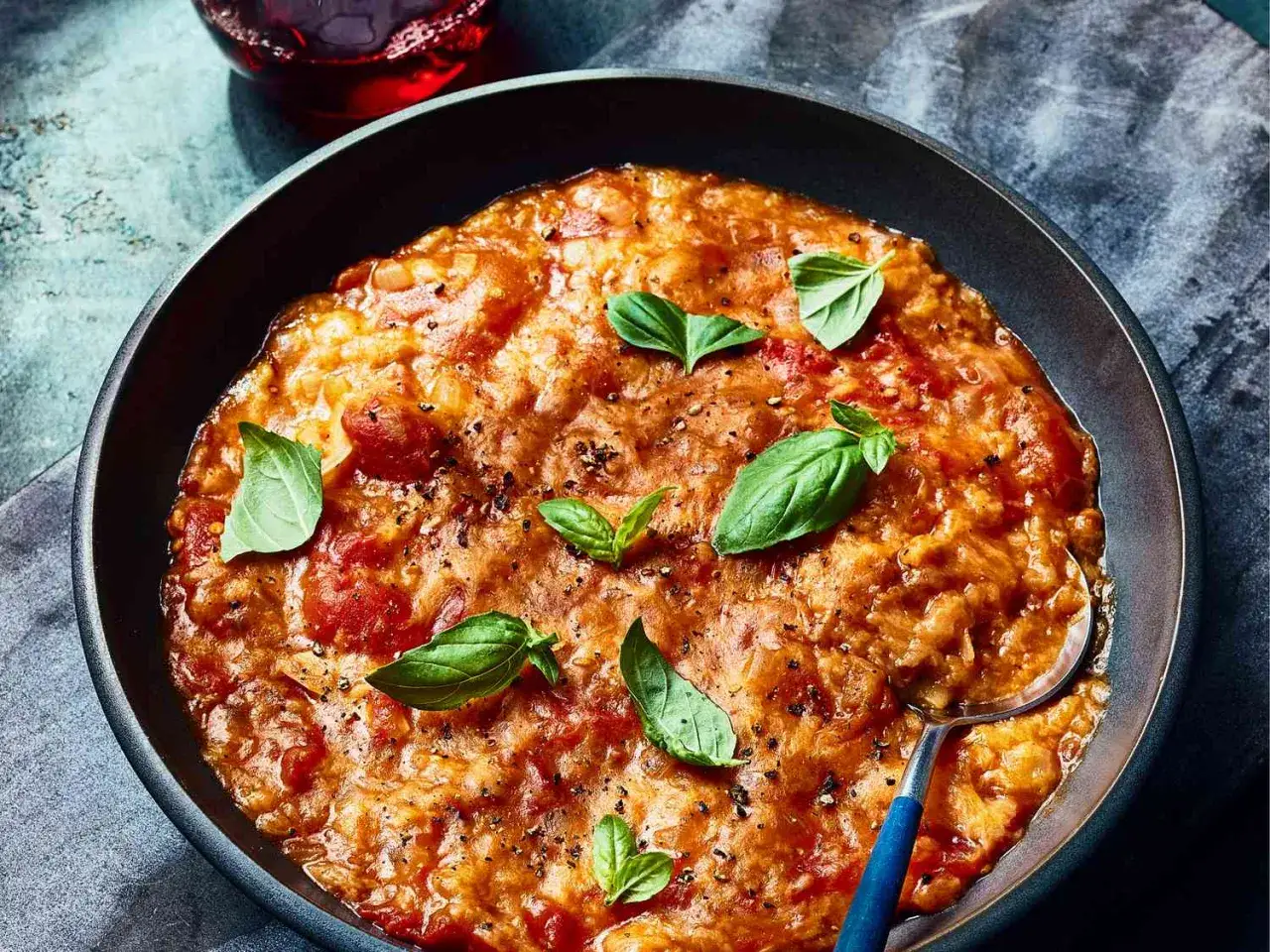 Un plat de ribollita toscana réconfortant, garni de feuilles de basilic frais et de poivre noir, servi dans un bol sombre.