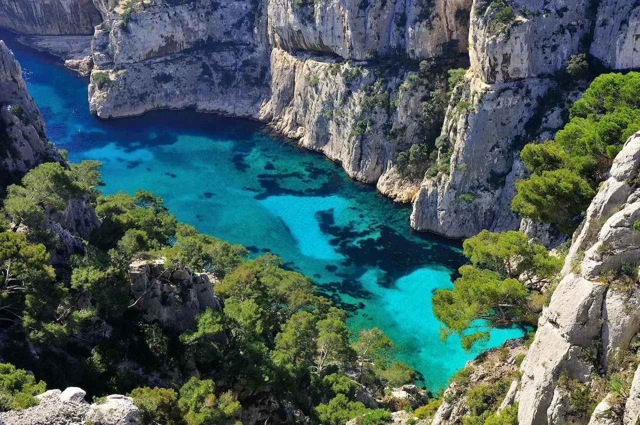 Vue aérienne d'une calanque aux eaux turquoise, un endroit paradisiaque en France, entourée de falaises calcaires et de pins verts.