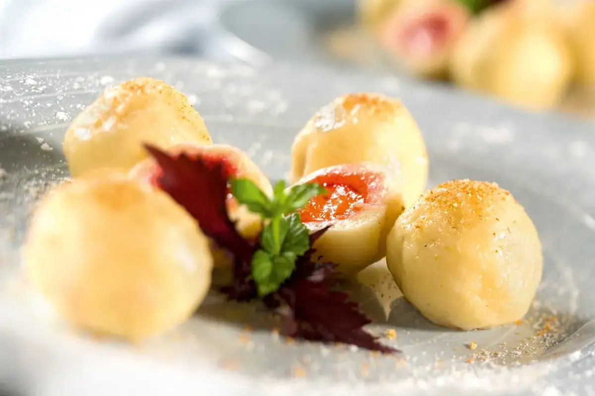 Boules de pâte moelleuses, garnies de confiture de fruits rouges, saupoudrées de chapelure et de sucre glace. Un délicieux dessert tchèque.