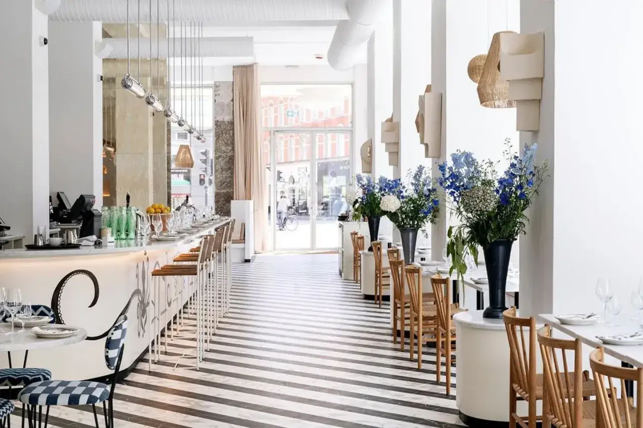Int&eacute;rieur lumineux d'un restaurant chic avec un long bar, des tables dress&eacute;es et des bouquets de fleurs bleues. Un aper&ccedil;u des meilleurs restaurants Copenhague.