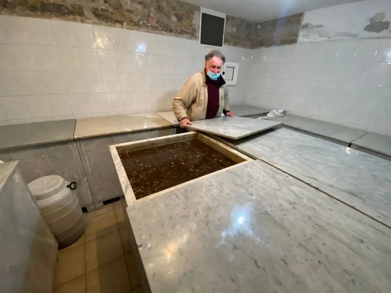 Un homme manipule un couvercle en marbre sur un bac rempli de liquide brun, peut-être pour le lard de Colonnata.