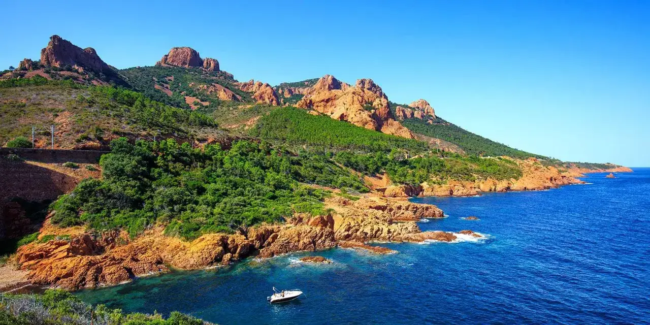 La côte rocheuse rouge de Saint-Raphaël, baignée par la mer Méditerranée, avec une petite bateau naviguant dans les eaux bleues.